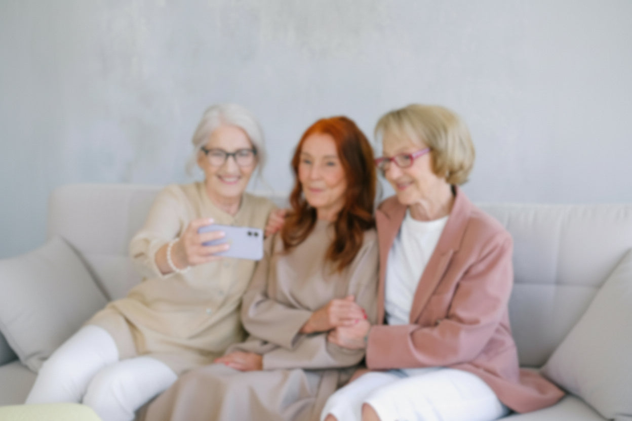 Three women sitting on a couch, taking a selfie with a smartphone.